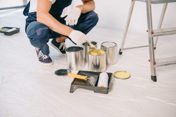 cropped view of painter taking yellow paint from can with paintbrush